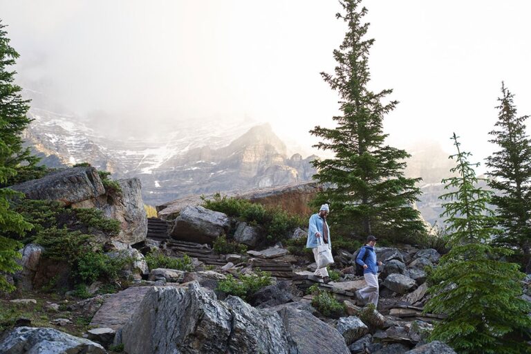 Two people walking down large rock steps in the foreground, mountains in the background